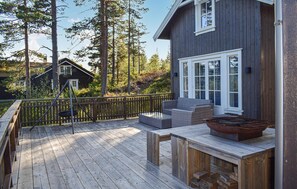 Une terrasse en bois avec des meubles d’extérieur, une balançoire et une vue sur une zone boisée.