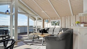 A spacious living area with a large gray sofa, a wooden coffee table, and a dining table with chairs. There is a large window providing a view of the outdoors. - Gorgeous home in Rømø with sauna (Rømø)