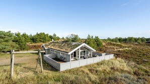 A white house with a sloped roof, situated on a grassy hill with trees in the background. - Gorgeous home in Rømø with sauna (Rømø)