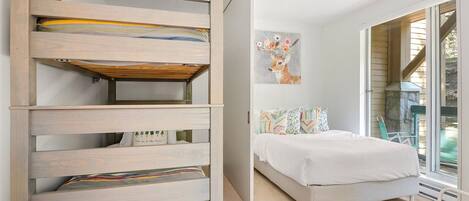 A bedroom with a bed, a built-in bench with storage, a painting on the wall, and a view of the outdoors.