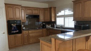 A kitchen with wooden cabinets, a microwave, a refrigerator, and a large island with stools.