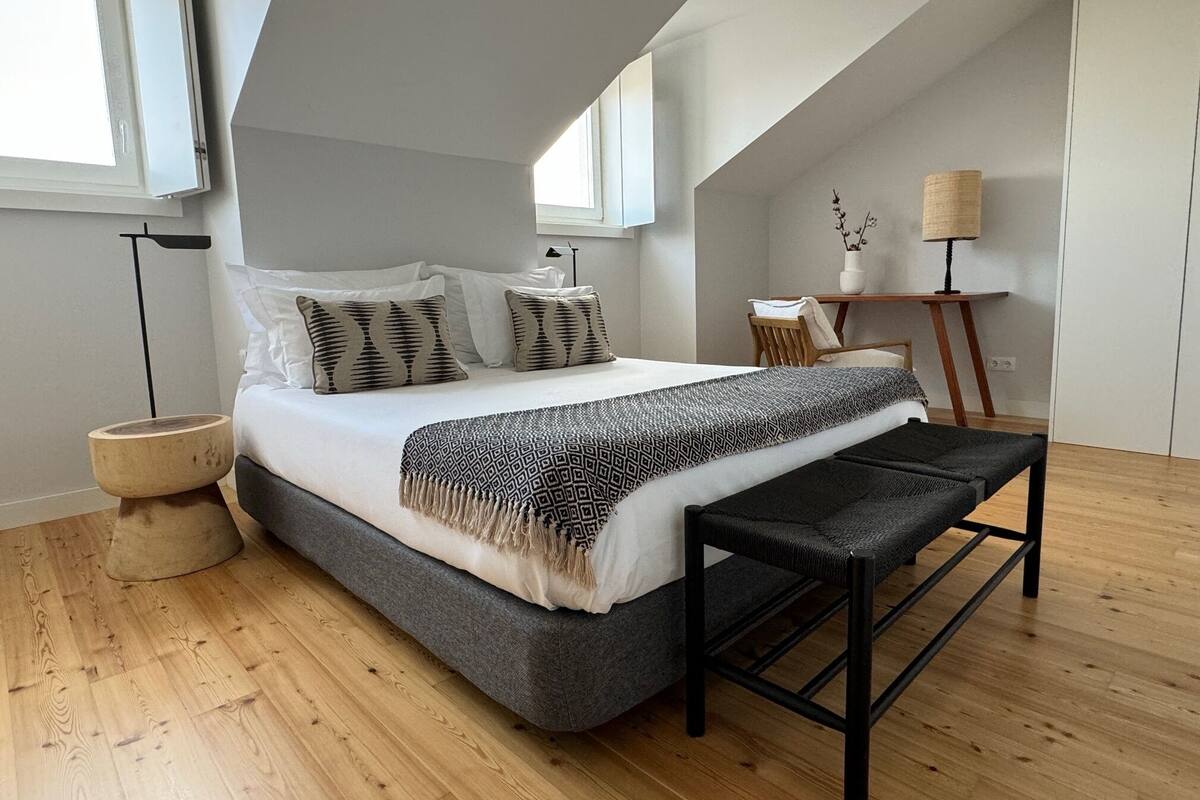 A modern bedroom with a large bed, a bench, a desk, and a lamp.