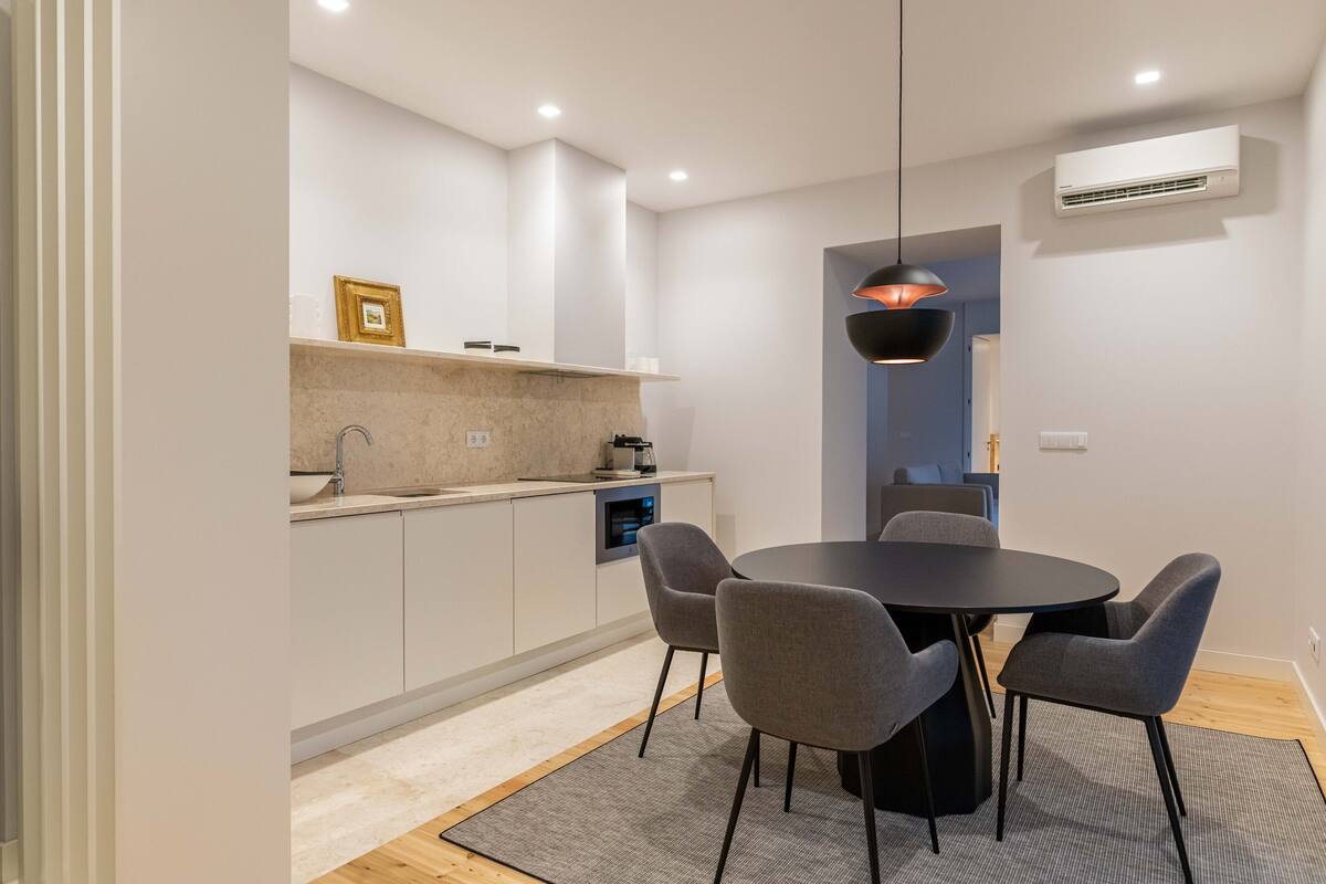 A modern kitchen with white cabinets, a black dining table, and four grey chairs.