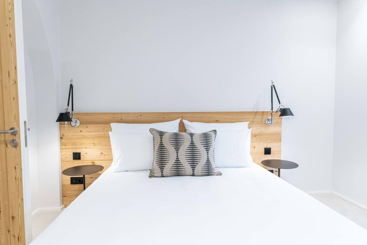 A bedroom with a wooden headboard, white bedding, two bedside tables, and a patterned pillow.