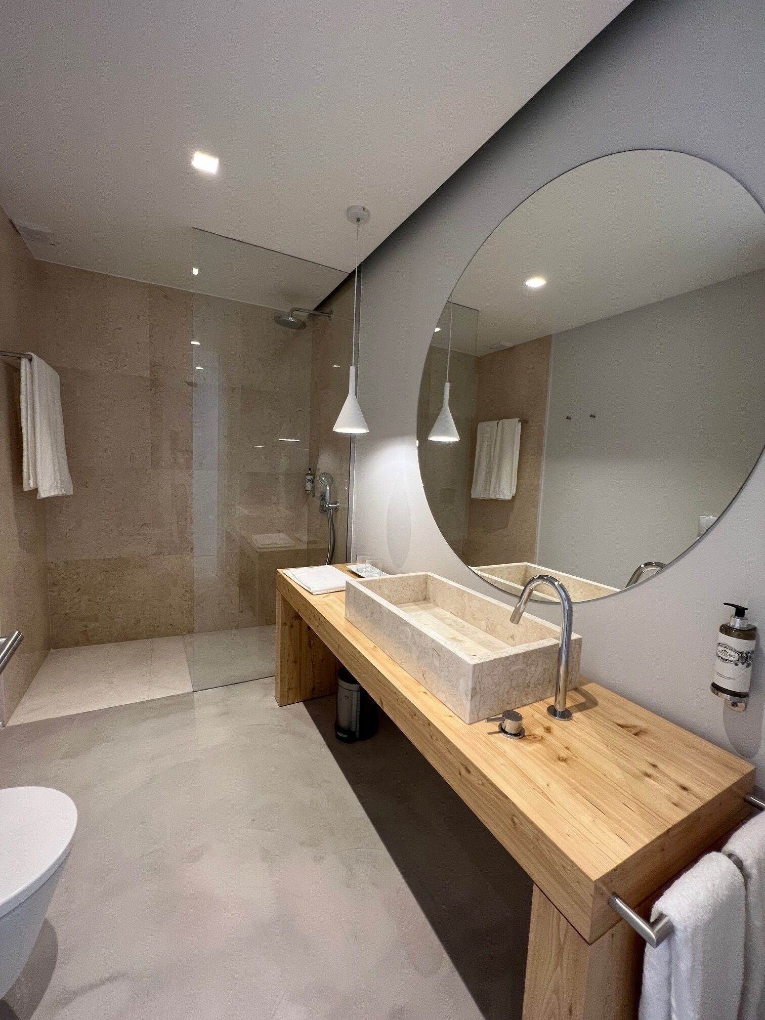 Een moderne badkamer met een houten wastafelmeubel, een grote spiegel, een douche en een toilet.