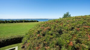 A coastal landscape with a grassy field, dense shrubbery, and a clear view of the sea with boats in the distance. - Awesome home in Broager with WiFi (Broager)