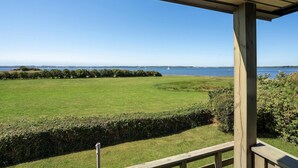 A view from a covered outdoor area with a wooden deck, overlooking a grassy field and a body of water with boats in the distance. - Awesome home in Broager with WiFi (Broager)