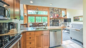 A kitchen with wooden cabinets, a stainless steel dishwasher, and a stone fireplace. - Lutsen Mountains Retreat w/ Resort Amenities! (Lutsen)