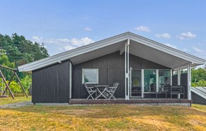 Un edifici modern amb un teulat inclinat, un porxo cobert amb taula i cadires, i una porta de vidre que dona a l'interior.