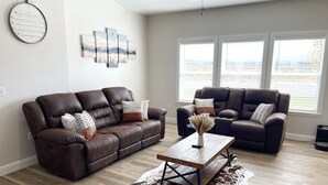 A spacious living room with two leather sofas, a wooden coffee table, and a large window offering a view of the outdoors. - 3 Peaks Mountain View Getaway w/Hot Tub! (Cedar City)