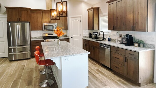 A modern kitchen with granite countertops, stainless steel appliances, wooden cabinets, and a central island with bar stools. - 3 Peaks Mountain View Getaway w/Hot Tub! (Cedar City)