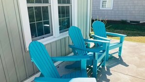Dos sillas Adirondack turquesa en un patio de hormigón junto a un edificio con detalles blancos y ventanas.