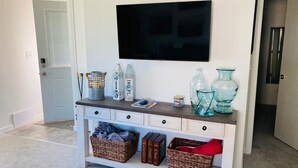 Una sala de estar con un televisor montado en la pared, una consola con cestas y adornos, y una puerta a la izquierda.