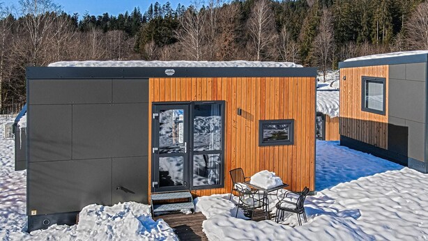Eine Holzhütte mit Glastür und einer kleinen Sitzgelegenheit im Freien.