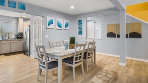 A modern kitchen with a built-in refrigerator, a dining area with a wooden table and chairs, and a staircase with a yellow accent. - Luxury 3-bedroom Tri-Level w/ Game Room (Hoquiam)