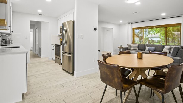 A modern kitchen with white cabinetry, a stainless steel refrigerator, and a dining area with a round wooden table and leather chairs. - Your Private Tropical Paradise with Heated Pool! (Sarasota)