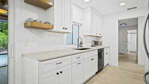 A modern kitchen with white cabinetry, wooden shelves, a sink, and a countertop. - Your Private Tropical Paradise with Heated Pool! (Sarasota)
