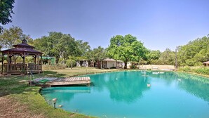 A clear blue swimming pool with a wooden deck, surrounded by grass and trees. - Lovely Pottsboro Home w/ Patio & Fire Pits! (Pottsboro)