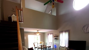 A spacious living area with a staircase, a ceiling fan, a flat-screen TV, and a dining area with chairs and a table.