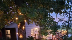 A wooden deck with a railing, a stone pathway, and a tree with lights.