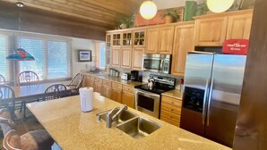 A kitchen with granite countertops, stainless steel appliances, wooden cabinets, and a bar area with stools. - Mountain Back (Mammoth Lakes)