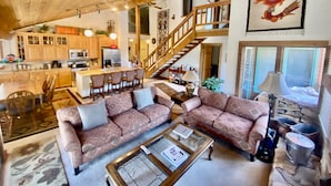 A spacious living room with a large sectional sofa, a glass coffee table, and a kitchen area with wooden cabinets and a central island. - Mountain Back (Mammoth Lakes)