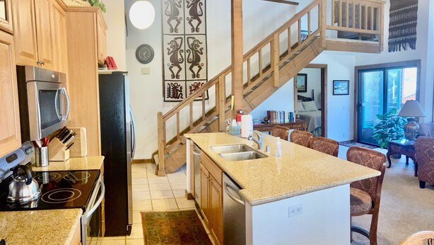 A kitchen with wooden cabinets, a built-in oven, and a microwave. There is a wooden staircase leading to a loft area. - Mountain Back (Mammoth Lakes)