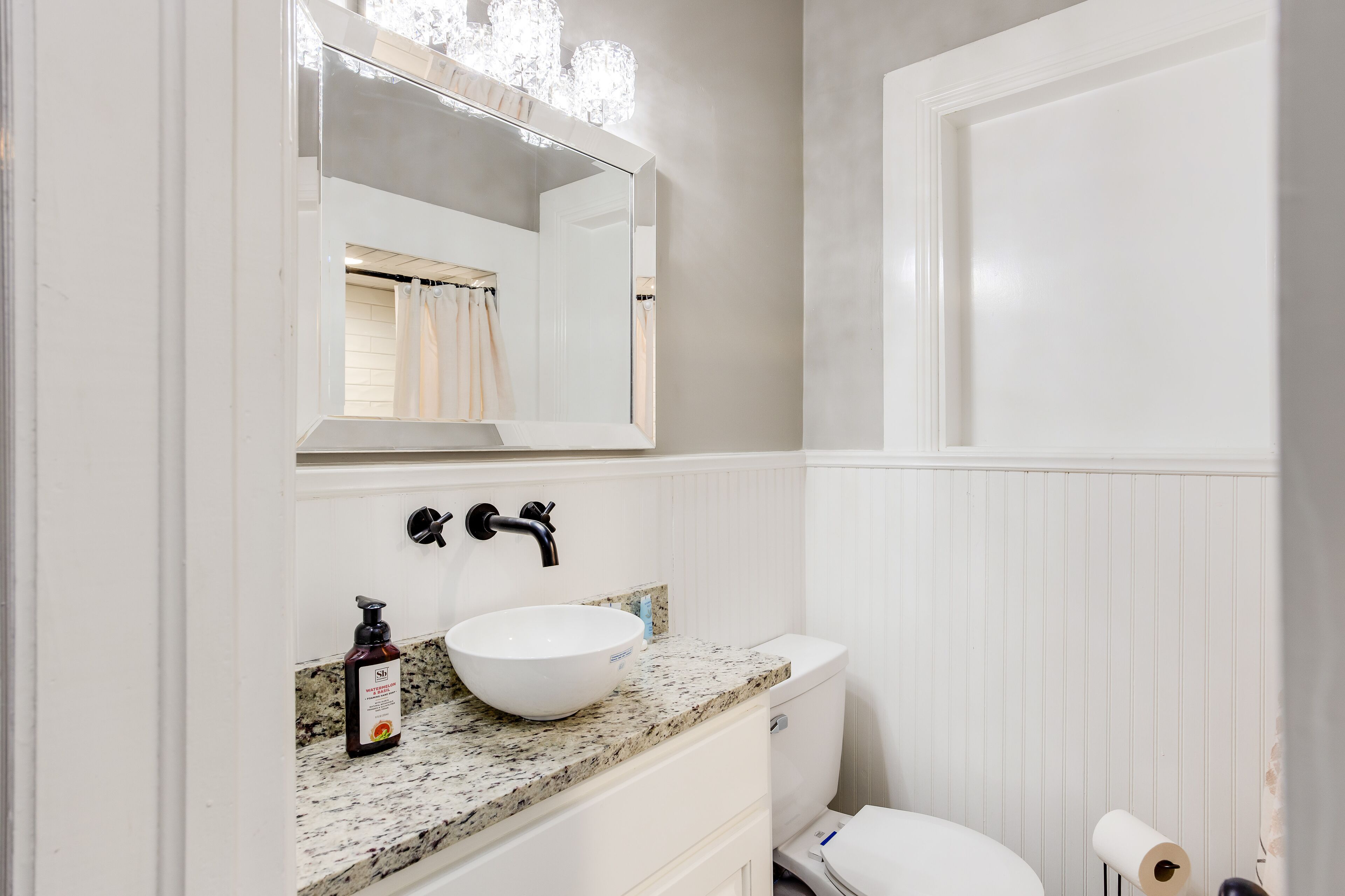 Une salle de bain avec un lavabo blanc, un miroir, des toilettes et un rideau de douche.