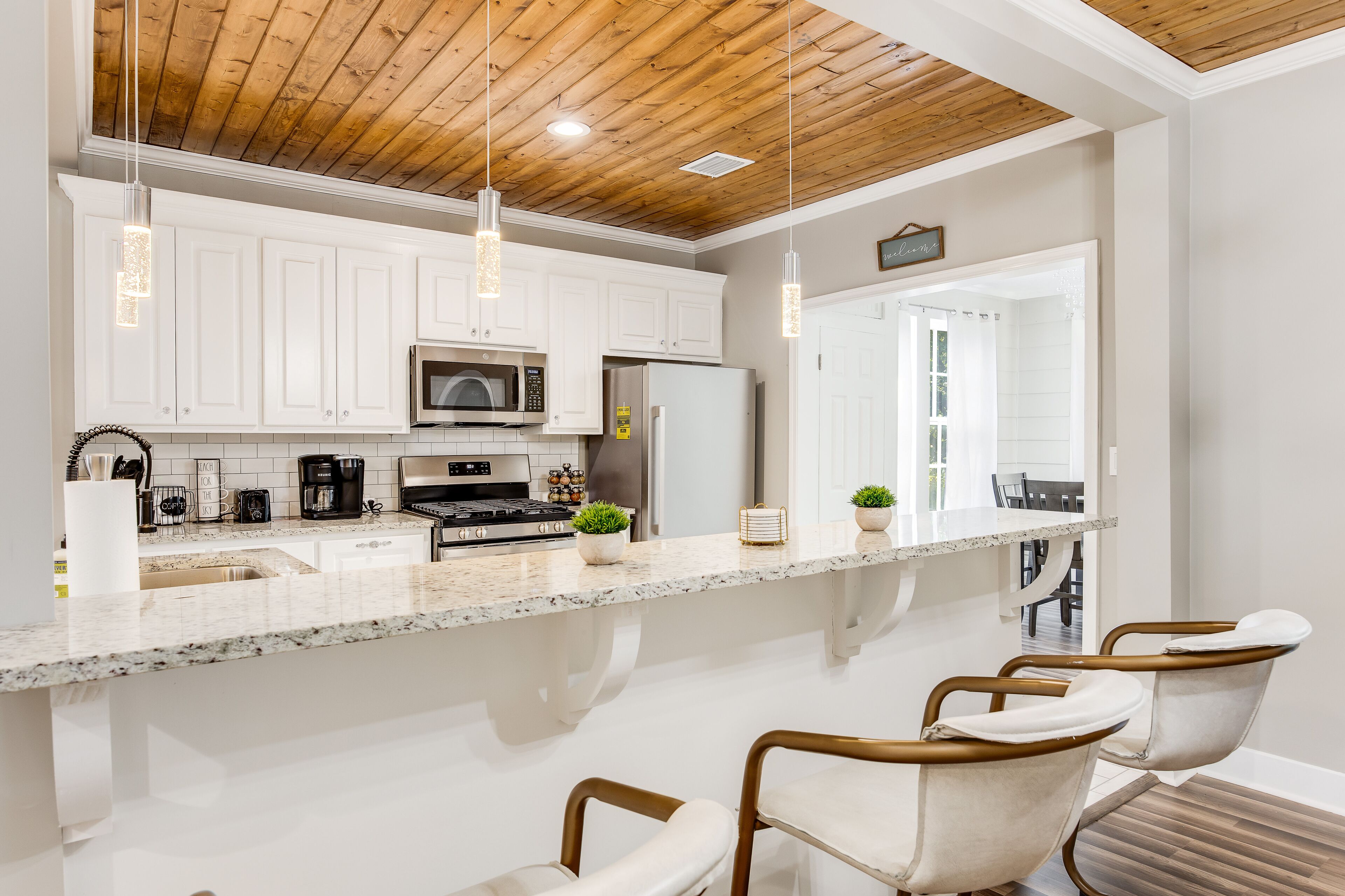A modern kitchen with white cabinets, granite countertops, and a wooden ceiling.