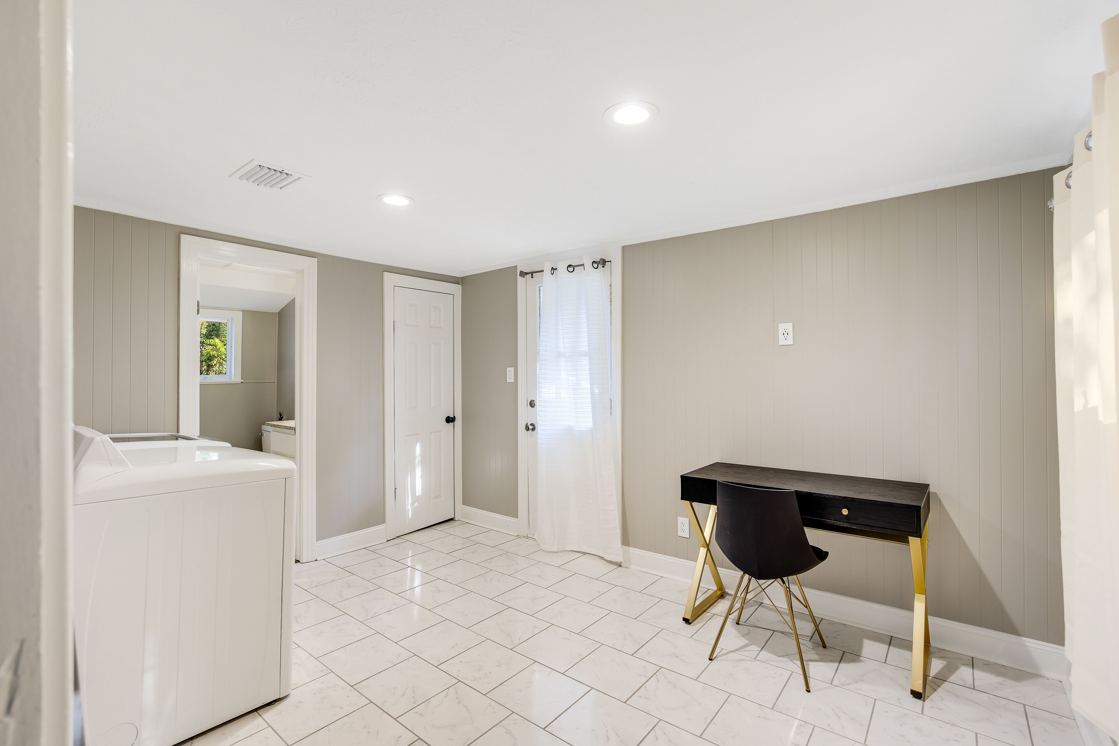 Une pièce avec un lave-linge blanc, un bureau noir aux pieds dorés et une porte blanche.