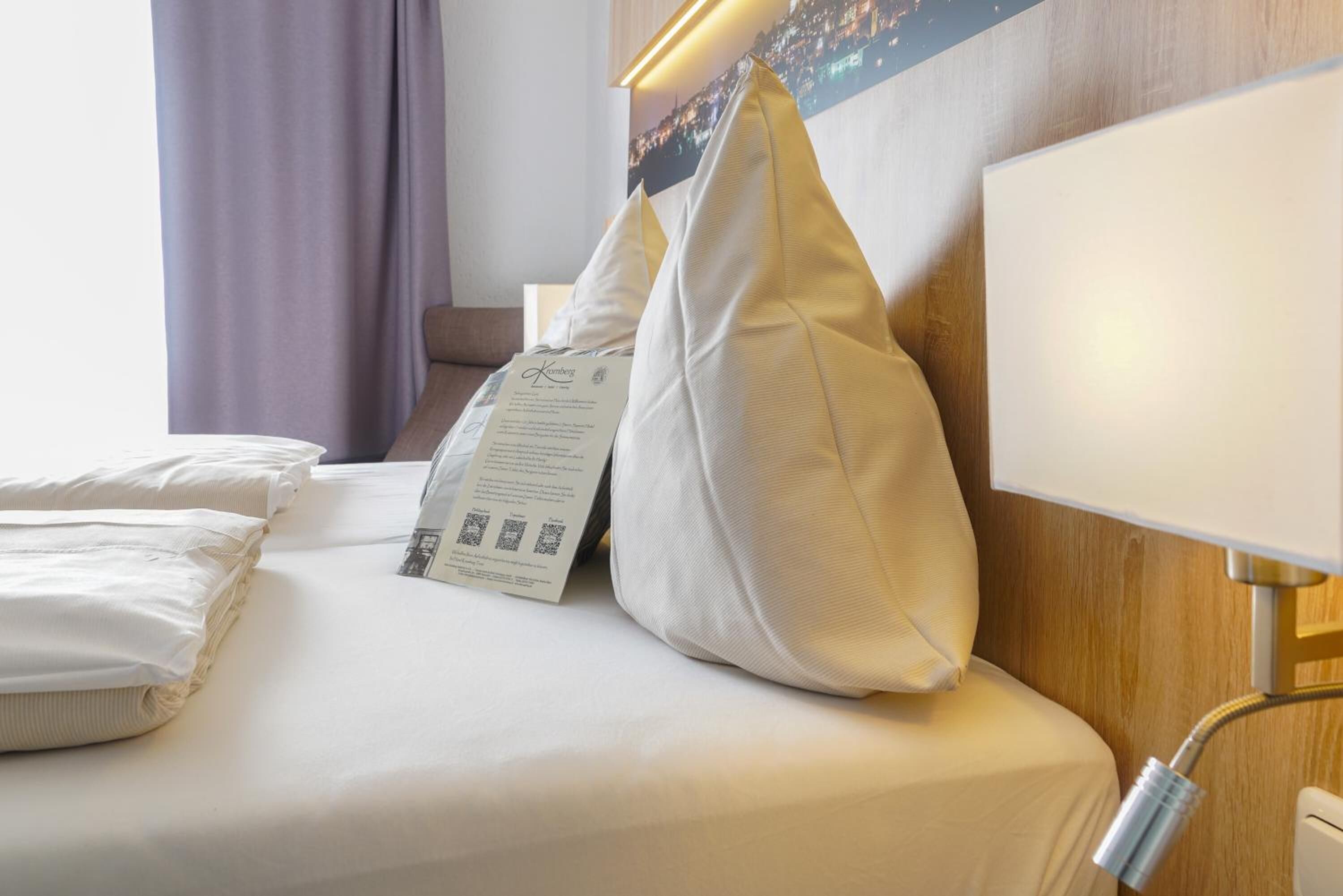 Un lit bien fait, avec du linge de lit blanc, un oreiller muni d’une étiquette et une lampe de chevet.