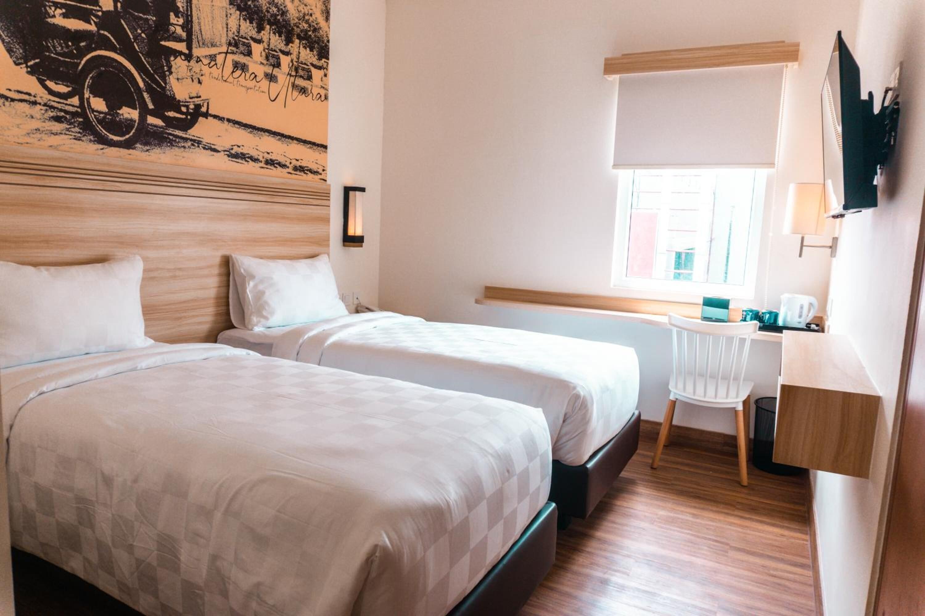Habitación de hotel con dos camas, un escritorio, una silla, una ventana con vistas y un televisor montado en la pared.