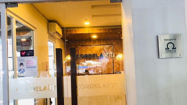 A hotel corridor with a wooden floor, glass doors, and a sign indicating management by OMEGA. - Cordela Inn Millennium Medan (Dwi Kora)