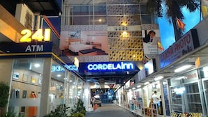 A commercial building with multiple storefronts, including an ATM, a business named 'CORDELAIM,' and a sign for 'Bleisure Travel Hotel.' - Cordela Inn Millennium Medan (Dwi Kora)