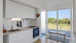 Una cucina moderna con mobili bianchi, un lavello in acciaio inox e un forno. È presente un'ampia porta scorrevole in vetro che dà su una terrazza con una panca in legno.