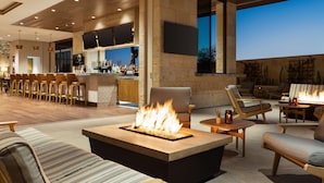 A spacious outdoor lounge area with a fire feature, comfortable seating, a bar with a view, and a stone wall.