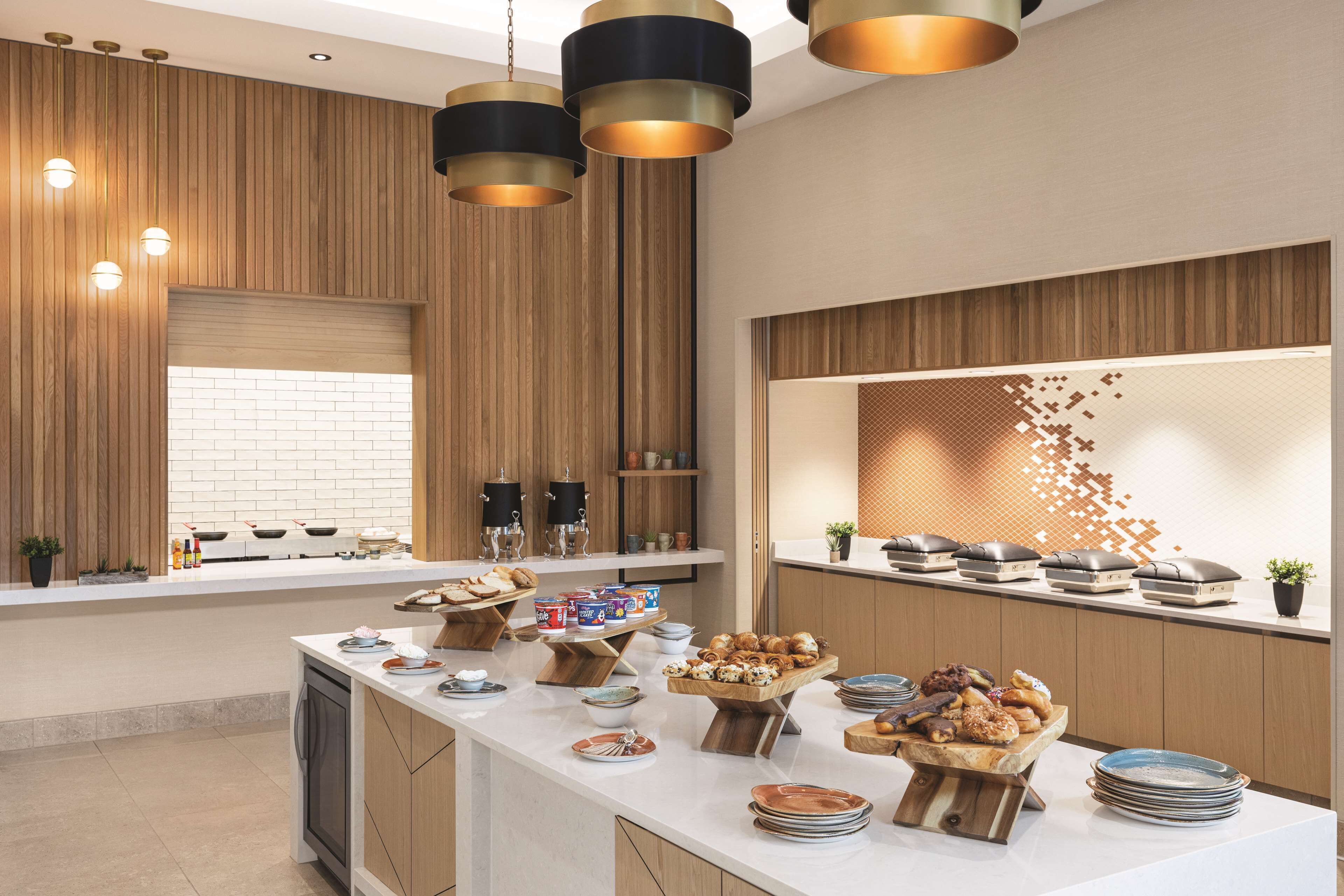 A modern kitchen with wooden paneling, a large island with food and drink items, and pendant lighting.