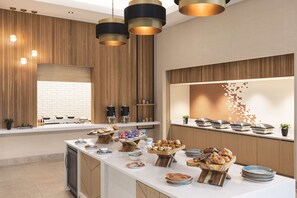 A modern kitchen with wooden paneling, a large island with food and drink items, and pendant lighting. - Hilton North Scottsdale At Cavasson (Scottsdale)