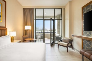 A hotel room with a large bed, a desk with a lamp, a chair, a sofa, and a balcony with a view. - Hilton North Scottsdale At Cavasson (Scottsdale)