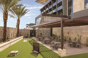 A hotel patio with outdoor seating, palm trees, and a stone wall. - Hilton North Scottsdale At Cavasson (Scottsdale)