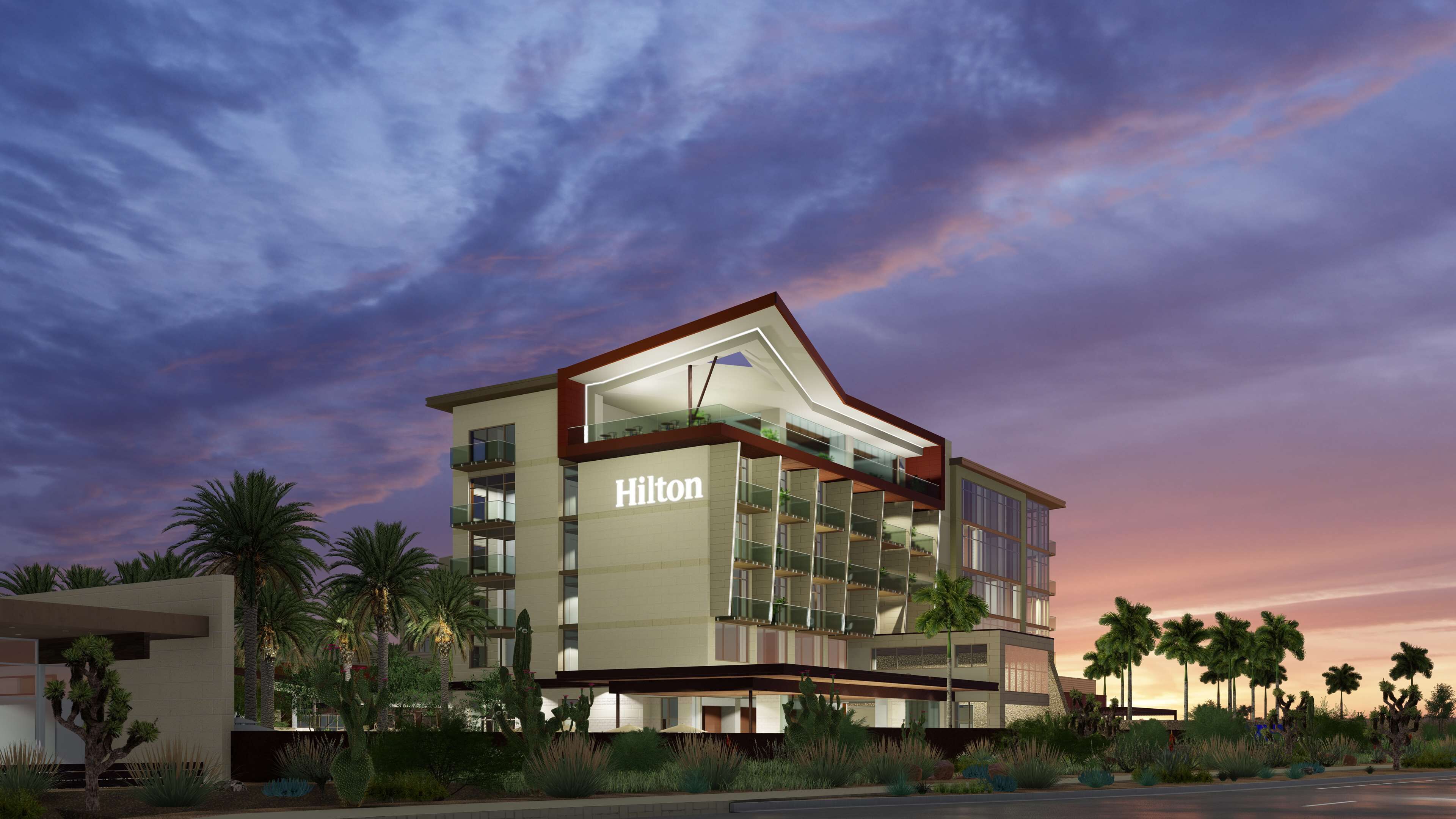 A modern Hilton hotel with a prominent 'Hilton' sign, multiple balconies, and a desert garden with cacti and palm trees.