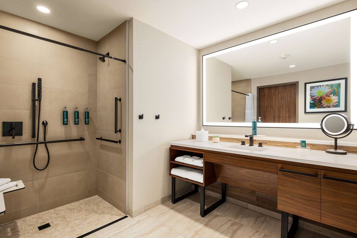 Ein modernes Badezimmer mit begehbarer Dusche, einem großen Spiegel und einem Waschtisch mit Spüle und Handtuchhalter.