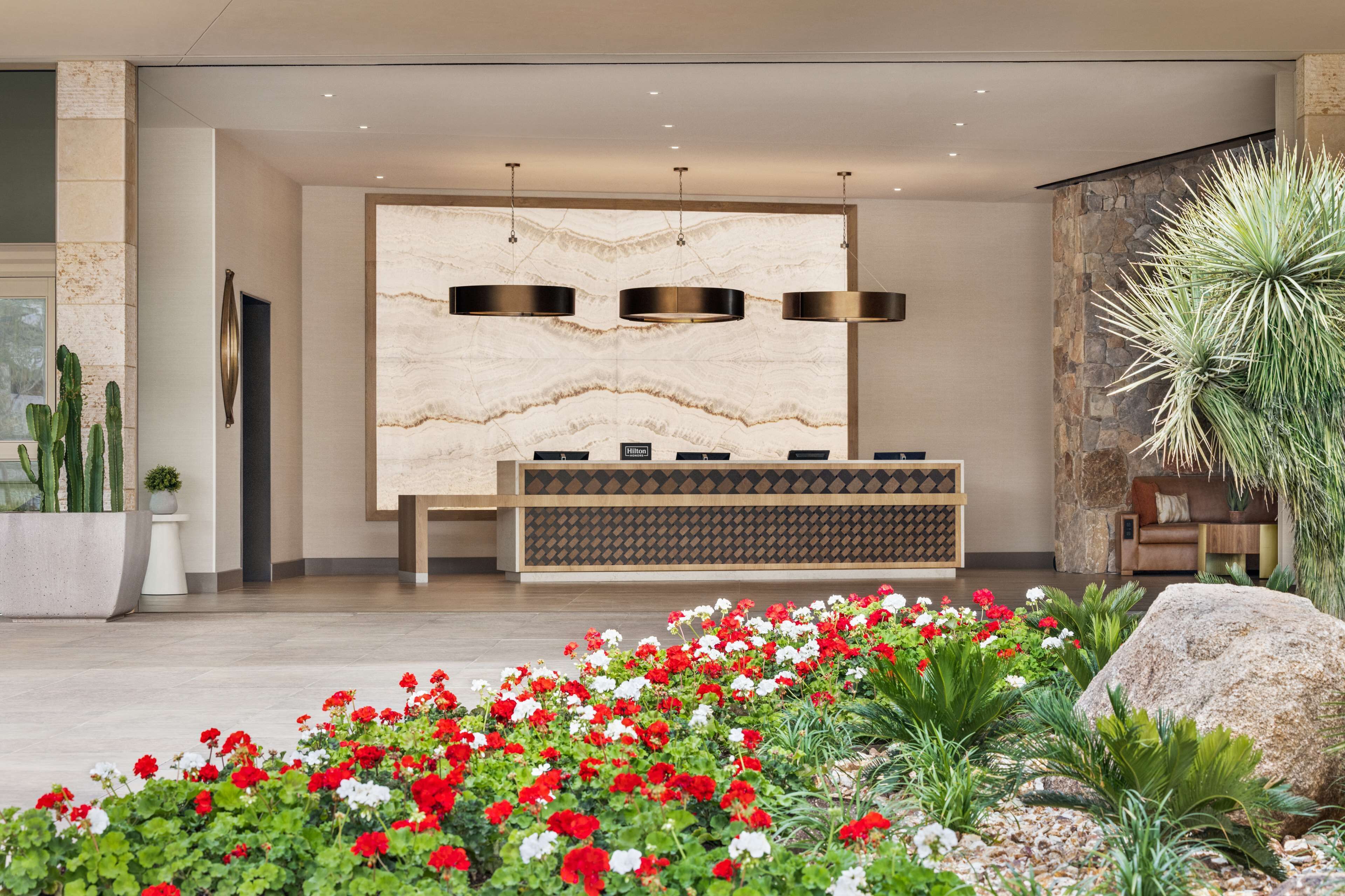 Un vestíbulo moderno con pared de mármol, un mostrador de recepción y diversas plantas.