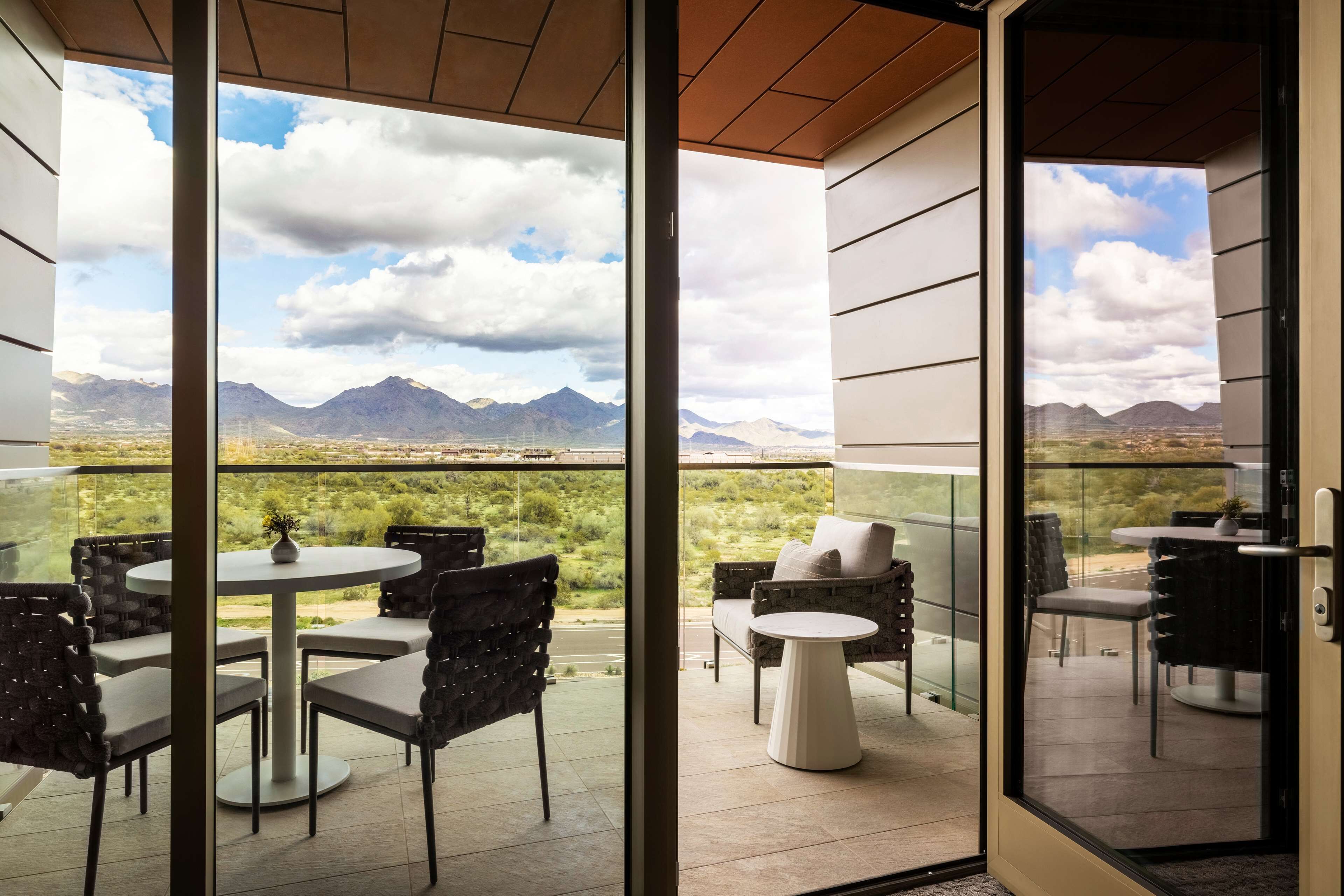 A balcony with a view of mountains and a clear sky. There are several chairs and tables arranged for outdoor dining.