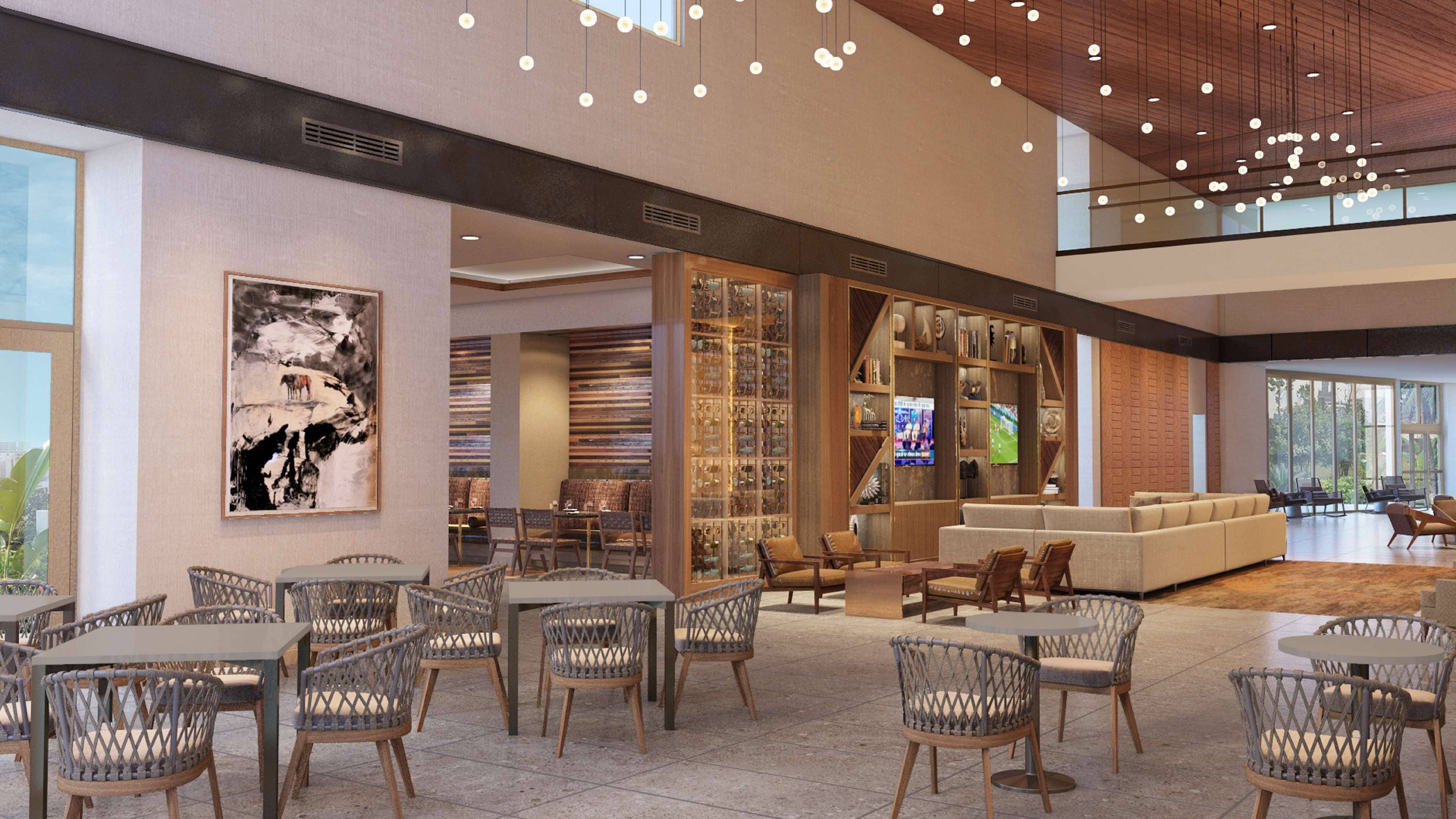 A spacious lobby with a high ceiling, modern lighting, a large seating area, and a wall with a collection of items.
