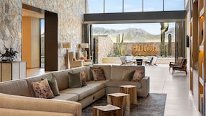 A spacious living area with a large sectional sofa, wooden coffee tables, and a stone wall.