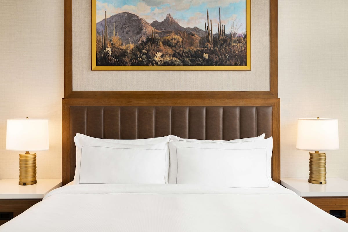 Ein Hotelzimmer mit einem großen Bett, zwei Nachttischen mit Lampen und einem gerahmten Landschaftsbild über dem Bett.