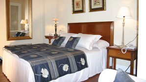 Una cama bien hecha con colcha azul y blanca, un cabecero de madera y una mesita de noche con una lámpara y un teléfono.