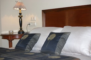 Une chambre d’hôtel avec une tête de lit en bois, une table de chevet avec une lampe et deux coussins décoratifs.