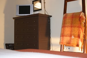 Une chambre avec un lit, une commode dotée de nombreux tiroirs, un téléviseur posé sur le dessus et une lampe.